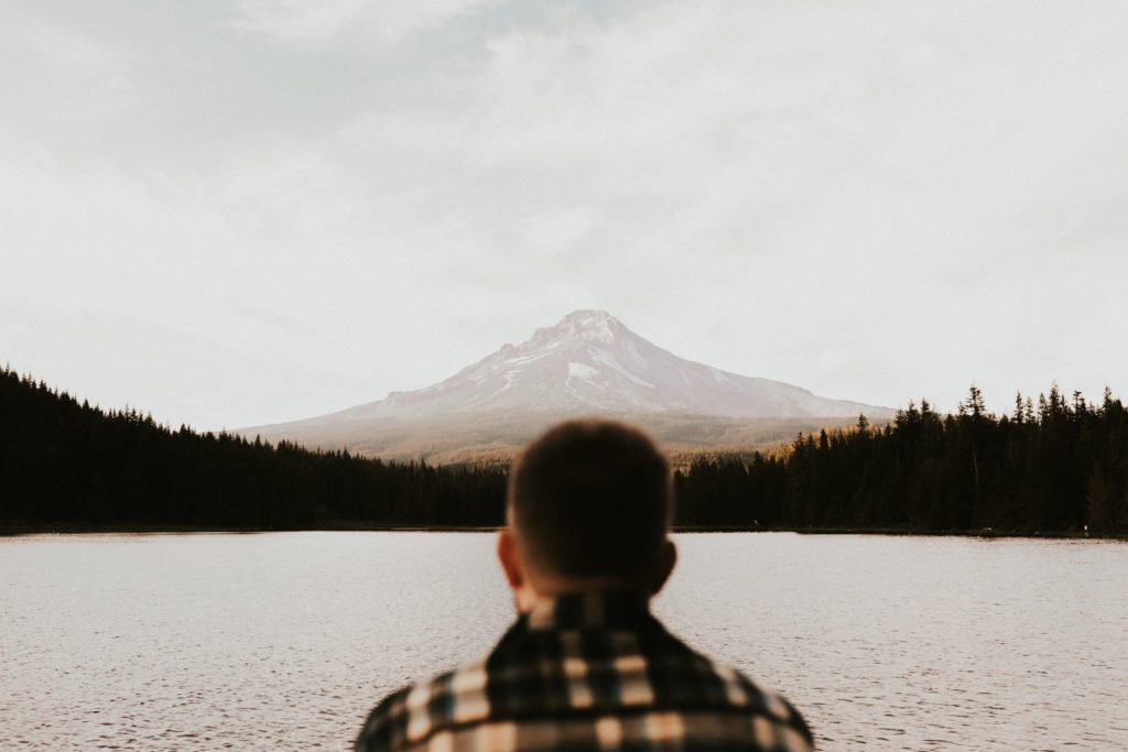 Man sitting in front of a lake with mountain in the background